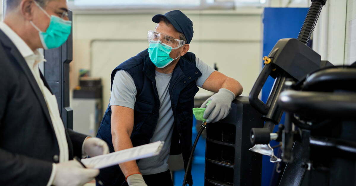 Auto repairman and his manager wearing protective face masks while talking in a workshop.
