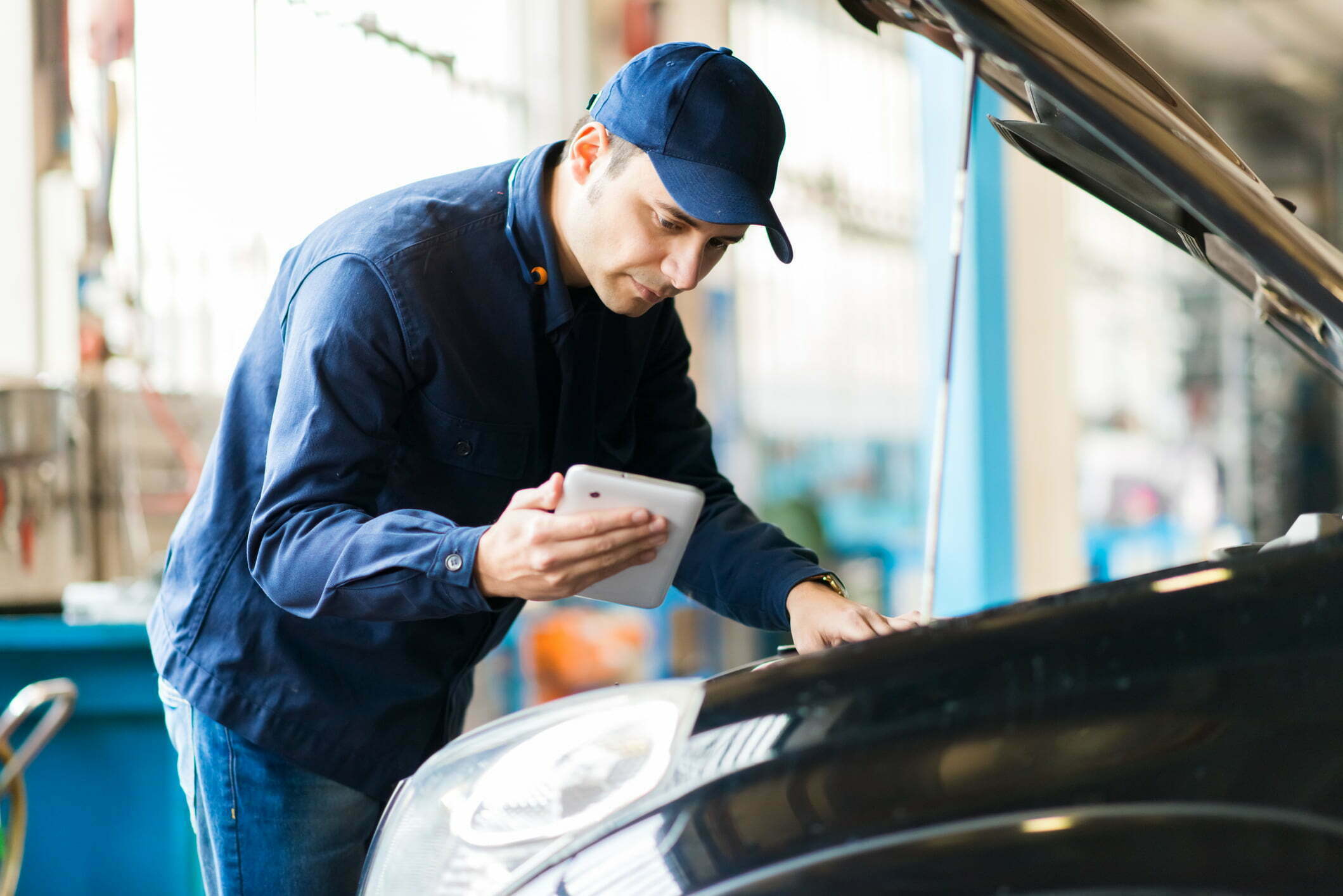 Man looking at tablet while trying to fix his car